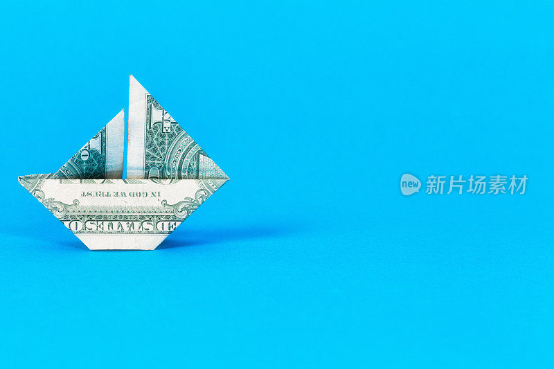 在浅蓝色的背景上，一张美元纸币折纸成一个纸船