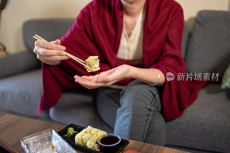 在家吃带酱料的塑料包装寿司卷的妇女