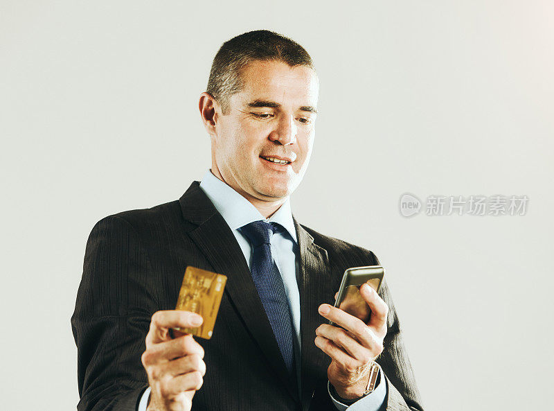 40多岁的帅哥手里拿着一张信用卡，满意地低头看他的手机