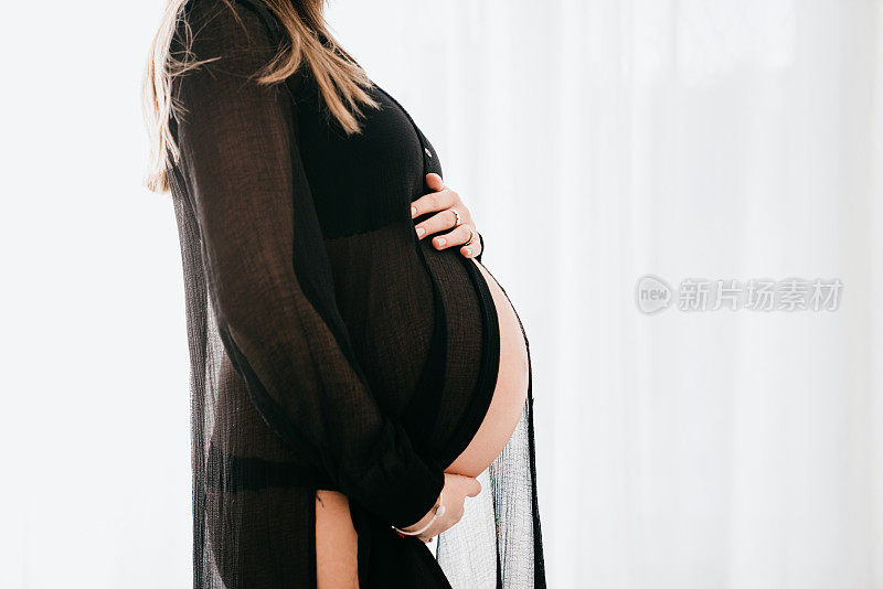 一名孕妇在白色背景下抚摸着自己的腹部