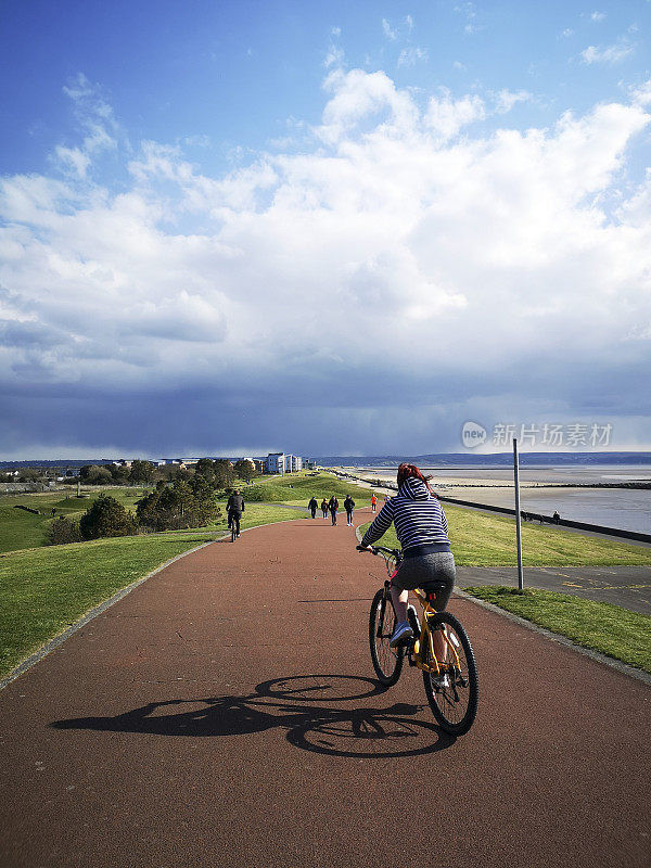 成年女性骑自行车在沿海的道路上-英国