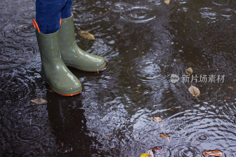 孩子们穿着胶靴在雨中的秋天水坑里。