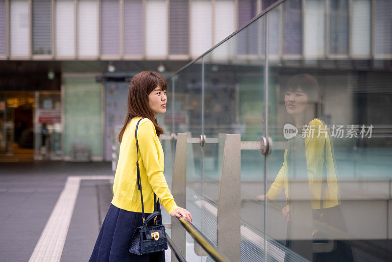 穿着黄色羊毛衫的日本女人从人行道上看风景