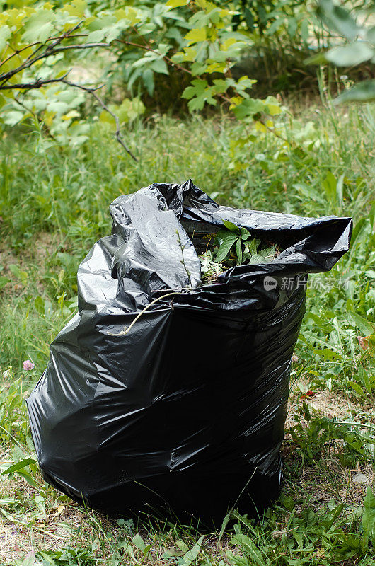 草地上放着一个装着垃圾的黑色塑料袋。垂直的摄影。