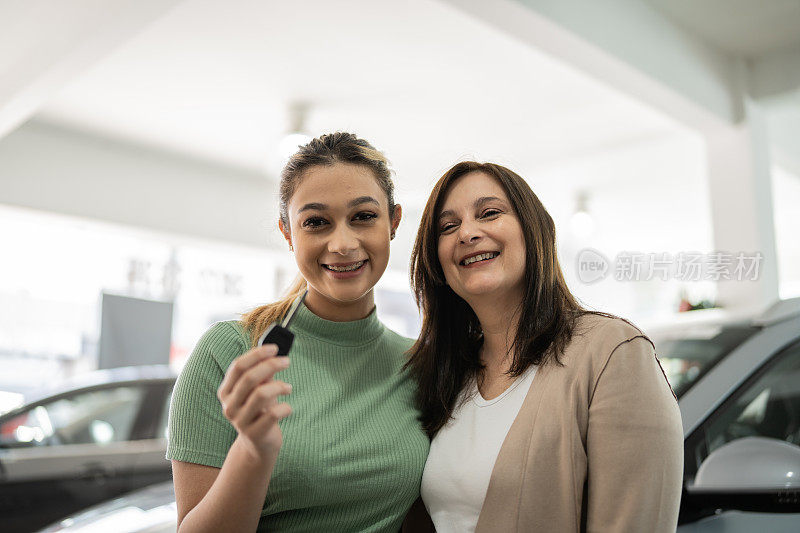 一个十几岁的女孩和她的母亲在汽车经销店展示新车钥匙的肖像