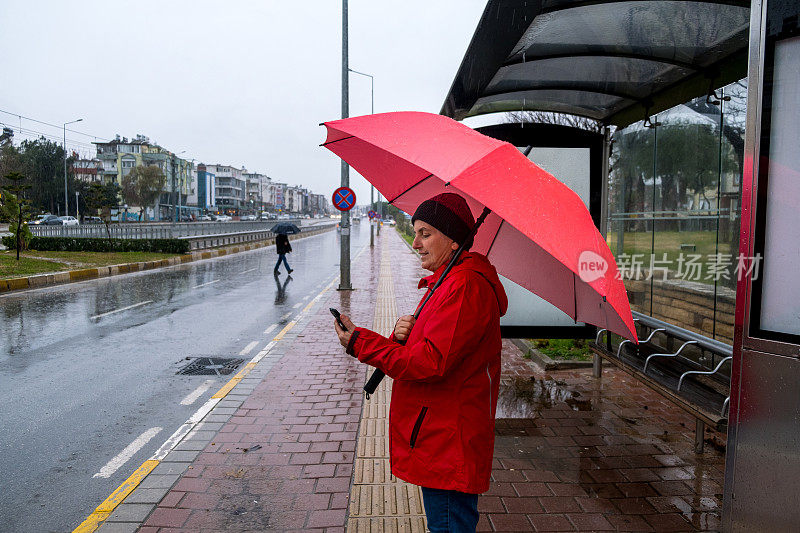 一位女士在雨天撑着伞在公共交通车站等车