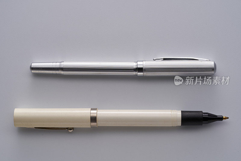 银色的钢笔和白色的圆珠笔在灰色的背景