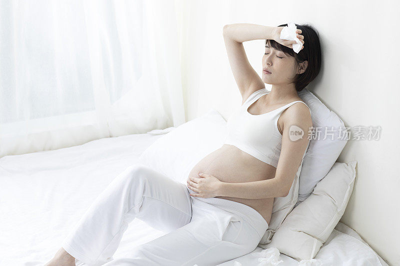 孕妇手摸肚子痛苦地坐在床上