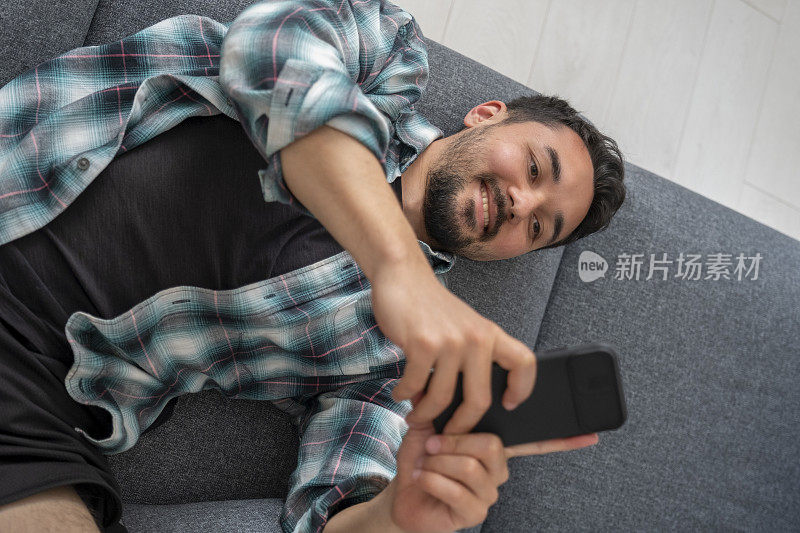 一个年轻人躺在沙发上用手机发短信