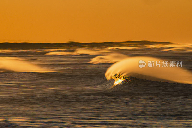 海浪的海景，强风浪花反射出海滩上明亮的金色日出