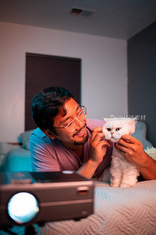 男人和猫在床上用投影仪看电影