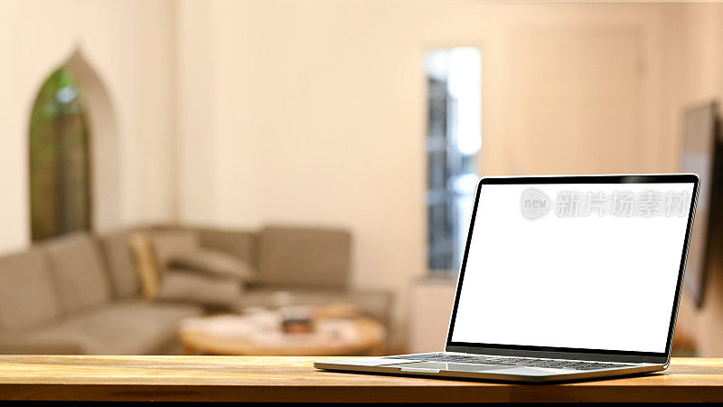 木桌子上的笔记本电脑，背景是模糊的现代客厅。空显示您的广告文本。