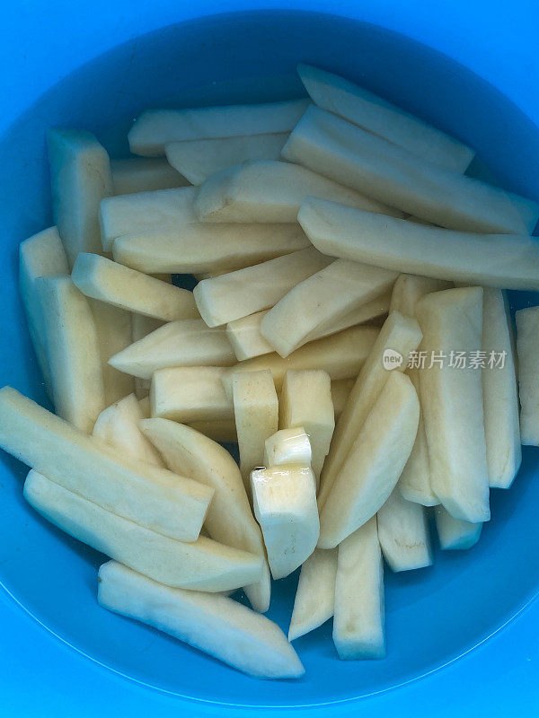 塑料的特写图像，蓝色的碗里装着切碎的生土豆，淀粉从切片的生土豆中浸泡出来，高架视图