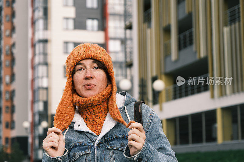 在多风的城市街道上戴着针织帽的快乐的妇女的腰部肖像