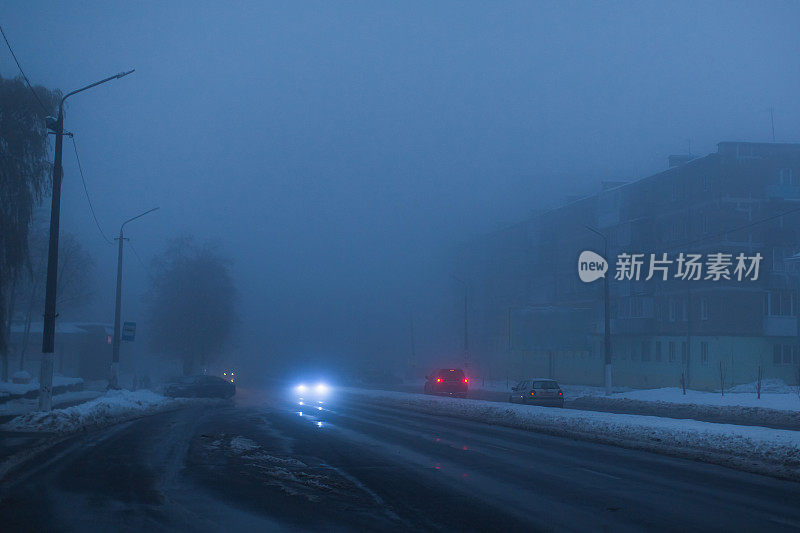 多雾的天气。夜雾。路面能见度低。汽车的运动。交通堵塞。湿滑的沥青。汽车头灯。一缕光。路上有冰雪。城市街道