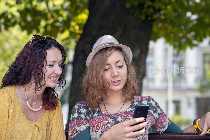 两个女孩坐在公园的长椅上用智能手机