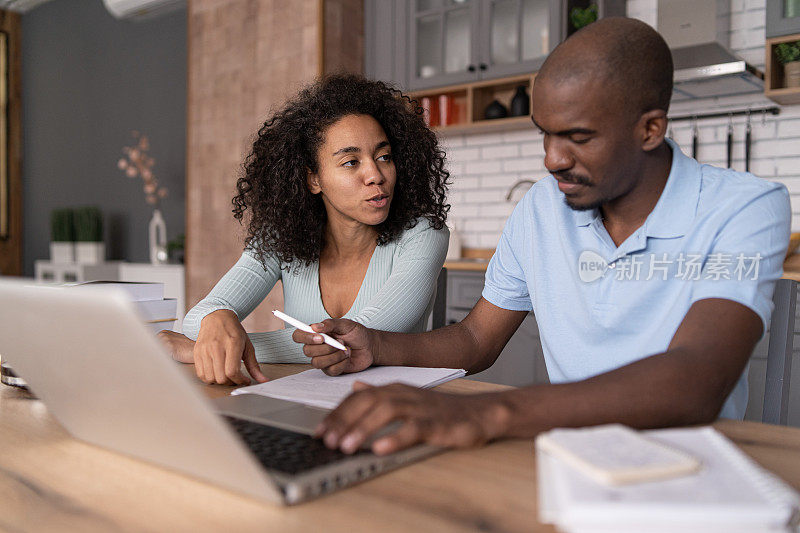 现代年轻的非裔美国夫妇观看在线学习课程，坐在厨房里，做笔记和讨论，电子学习的概念