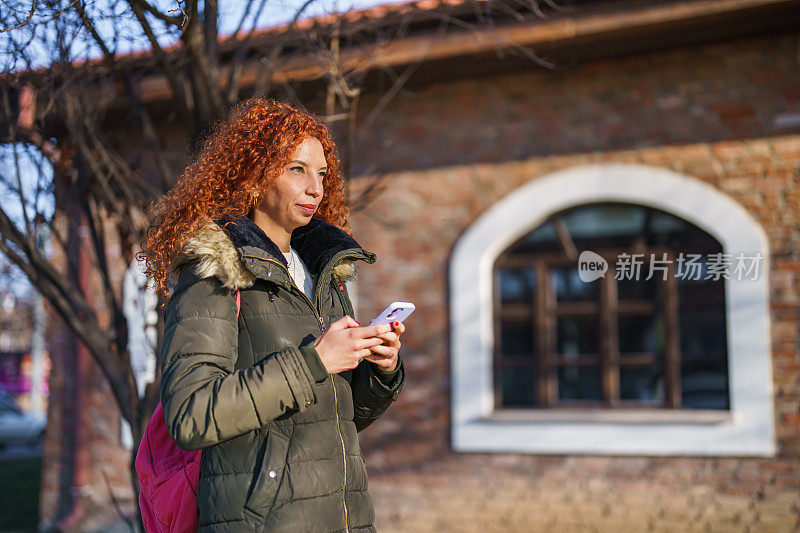 在一个阳光明媚的冬日，一名女子在户外边走边用智能手机