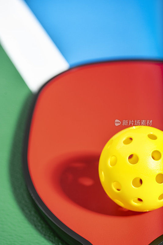 一个红色的匹克球球拍和一个黄色的球放在球场上