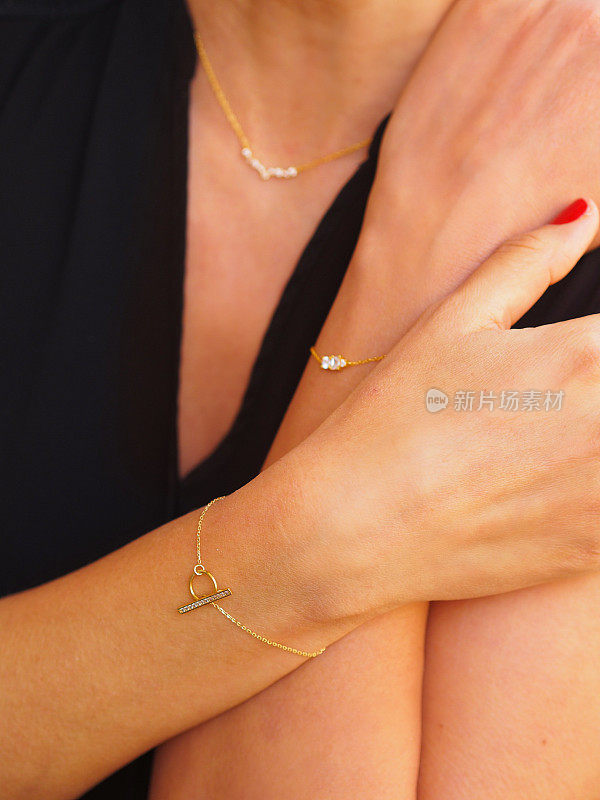 金钻石手镯戴在女人手腕上，双臂交叉在黑色上衣上