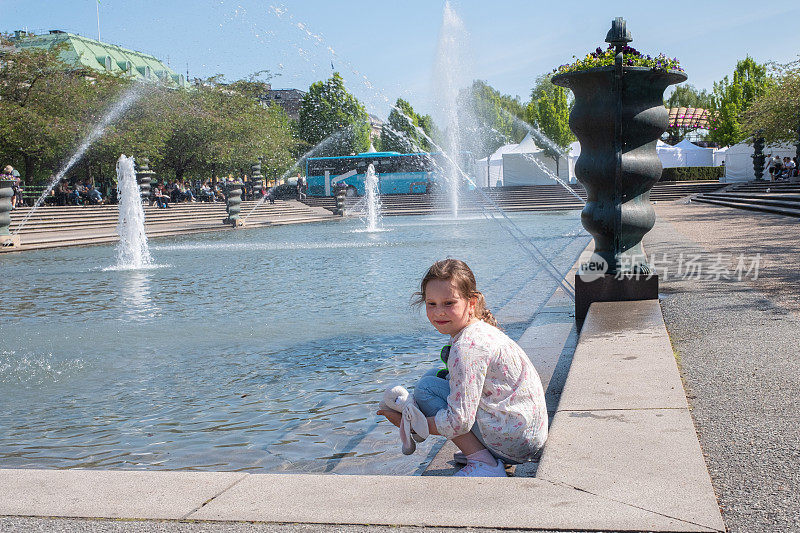 一个7岁的白人女孩在斯德哥尔摩城市喷泉附近的城市公园里休息。在阳光明媚的日子里散步。