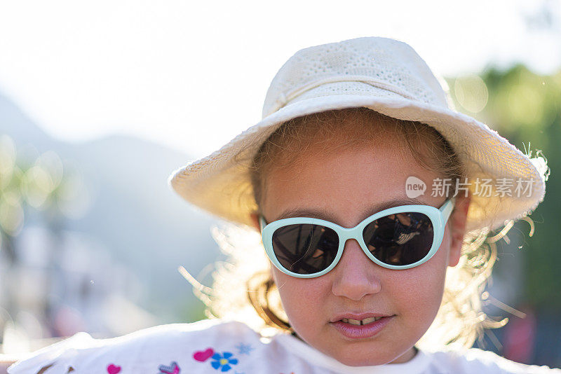 一个戴着帽子和太阳镜的女孩在海滩上的肖像