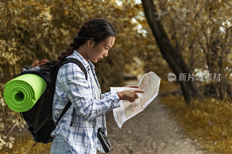 在林地徒步旅行的亚洲妇女手持地图指路