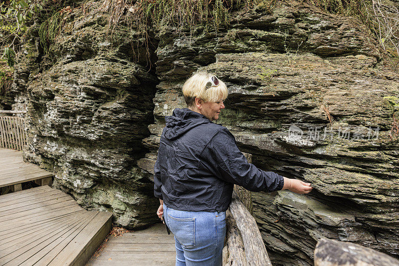 游客在宾夕法尼亚州布什金瀑布的徒步旅行路线。一个成熟的女人在宾夕法尼亚的波科诺山脉探索岩石