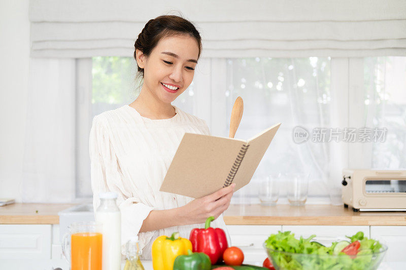 年轻女子在厨房里阅读烹饪书，寻找食谱