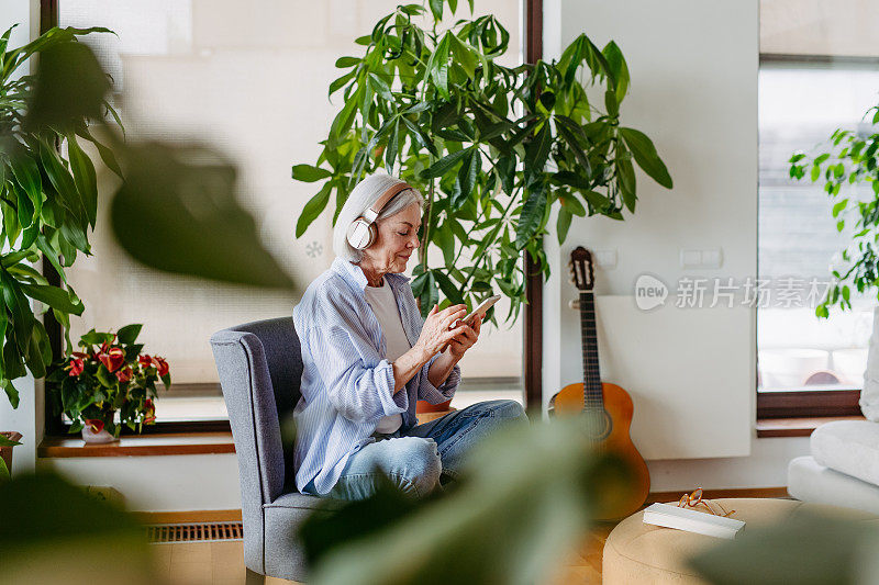 戴着耳机的老妇人，听着音乐，在家里放松。