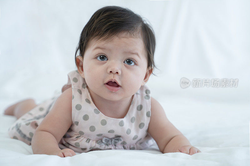 3个月大的新生婴儿躺在白色的床上。天真可爱的混血婴儿，亚洲人和高加索人，正在撒谎或爬行。小女孩在家里穿着可爱的衣服