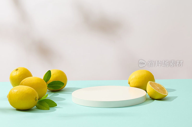 正面照片，一个空的圆形讲台放在淡蓝色的桌子上，白色的背景上有一些新鲜的黄色柠檬。展示空间