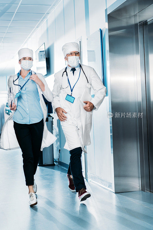 男女医生带着平板电脑和剪贴板在医院走廊里跑步