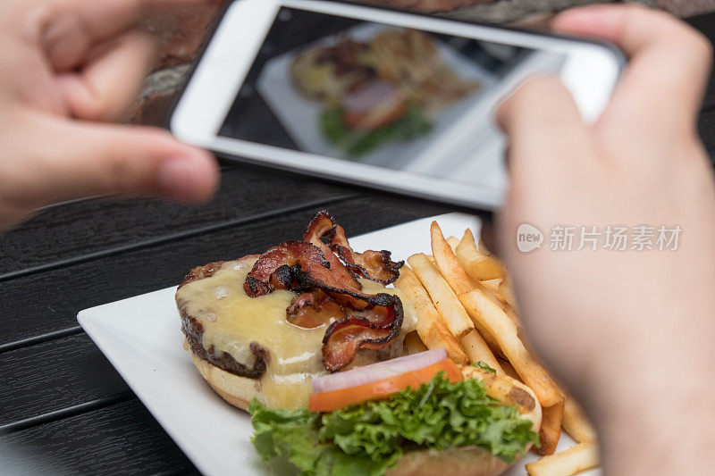 一名男子在户外酒吧用手机拍摄食物。用手机给食物拍张照片。汉堡，薯条，啤酒，白盘子，黑桌子，POV拍摄。