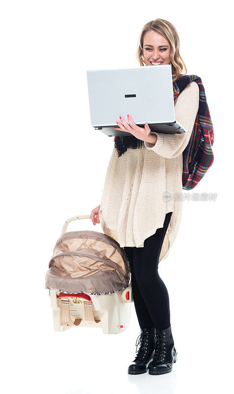 可爱的年轻妈妈抱着婴儿汽车座椅-抱着笔记本电脑