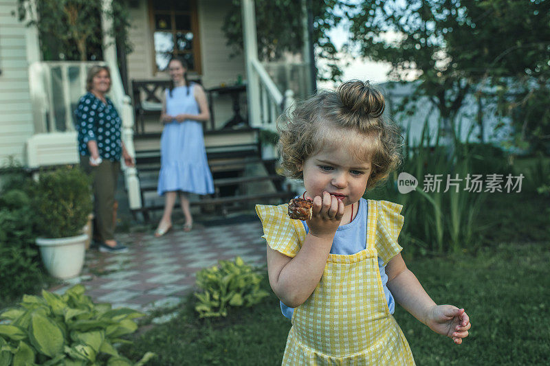 夏天，可爱的小女孩在她家后院附近吃饭，她的家人站在后面