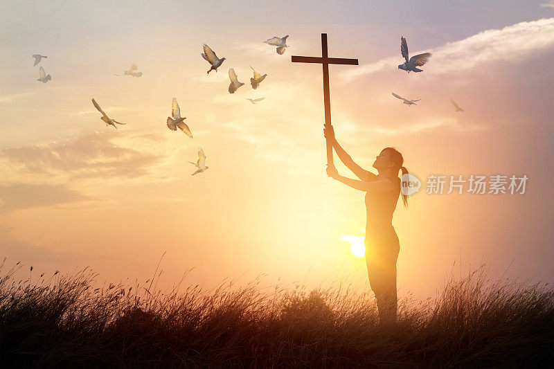 女人祈祷十字架和飞翔的鸟在日落的背景