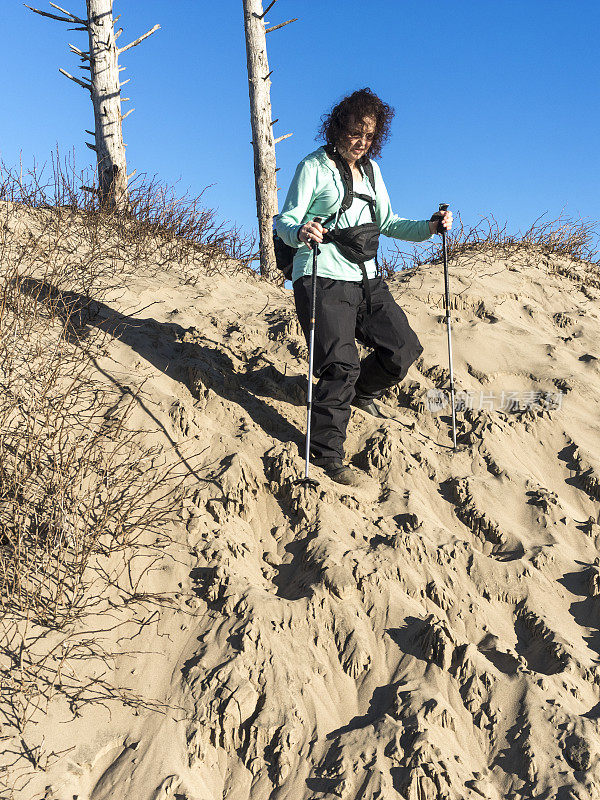 拿着登山杖的女人沿着太平洋城市的沙丘而下