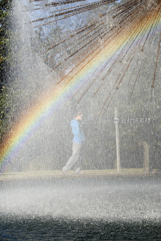 年轻的成年女性在彩虹后面喷水池