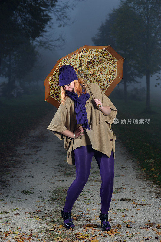 跳舞到秋天的女人在紫色的服装和伞