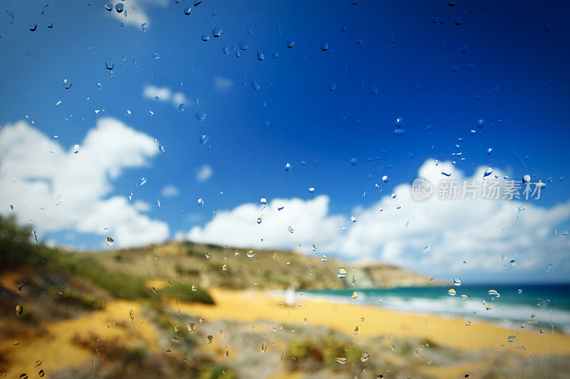 透过雨滴覆盖的窗户看到美丽的海滩