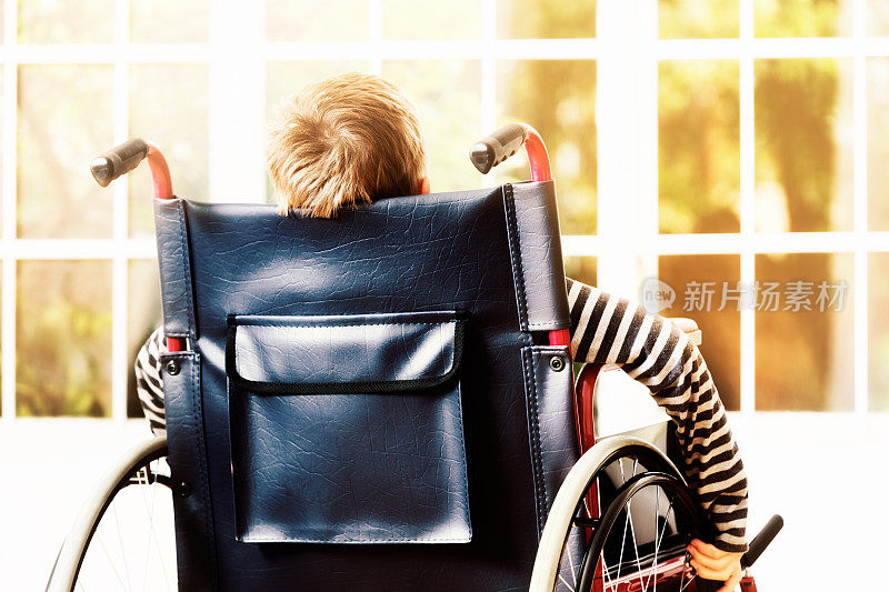小男孩推着轮椅走向阳光明媚的窗户