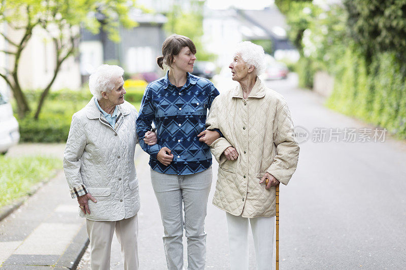 年轻的看护者帮助老年妇女在街上行走