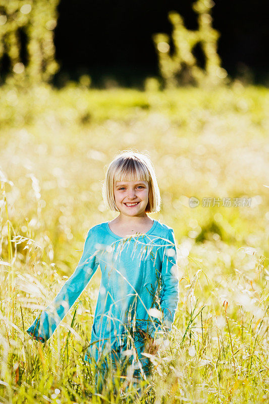 微笑的5岁金发女孩跑过长草