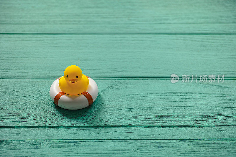 一只橡皮鸭放在一张旧的绿松石木桌上，上面有一个安全的充气环。