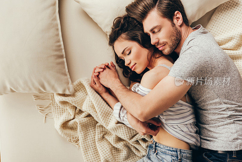 俯视图美丽的幸福的年轻夫妇拥抱而睡在床上