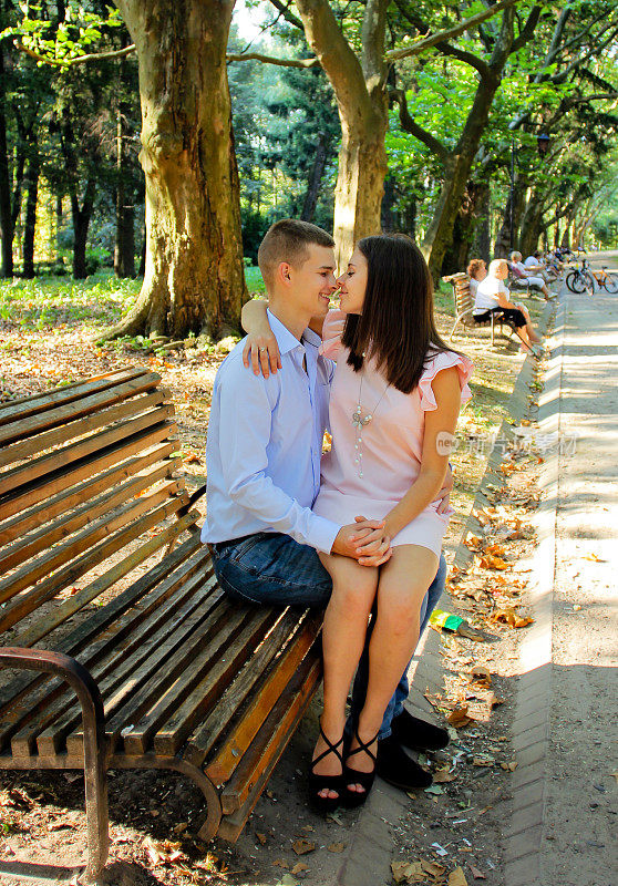 一对年轻夫妇坐在公园的木凳上，拥抱亲吻
