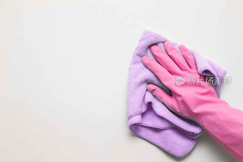 女人的手戴着粉色橡胶防护手套，用干抹布擦拭白色墙壁上的灰尘。早春大扫除或定期大扫除。女保洁员打扫房子。