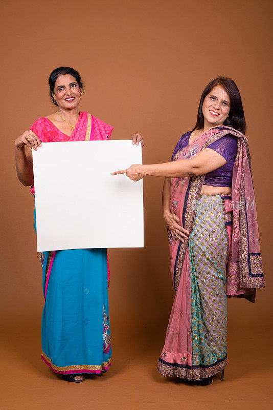 摄影工作室拍摄了两名成年印度妇女在彩色背景下一起穿着印度传统服装莎丽