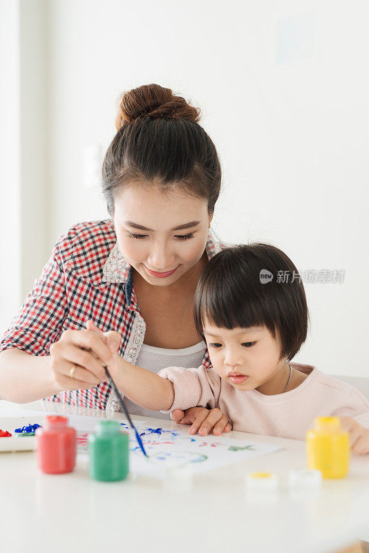 幸福的家庭妈妈和女儿一起画画。亚洲妇女帮助她的孩子的女孩。